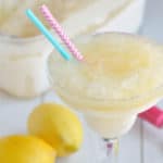 A close-up image of a glass of lemon vodka slush with 2 straws