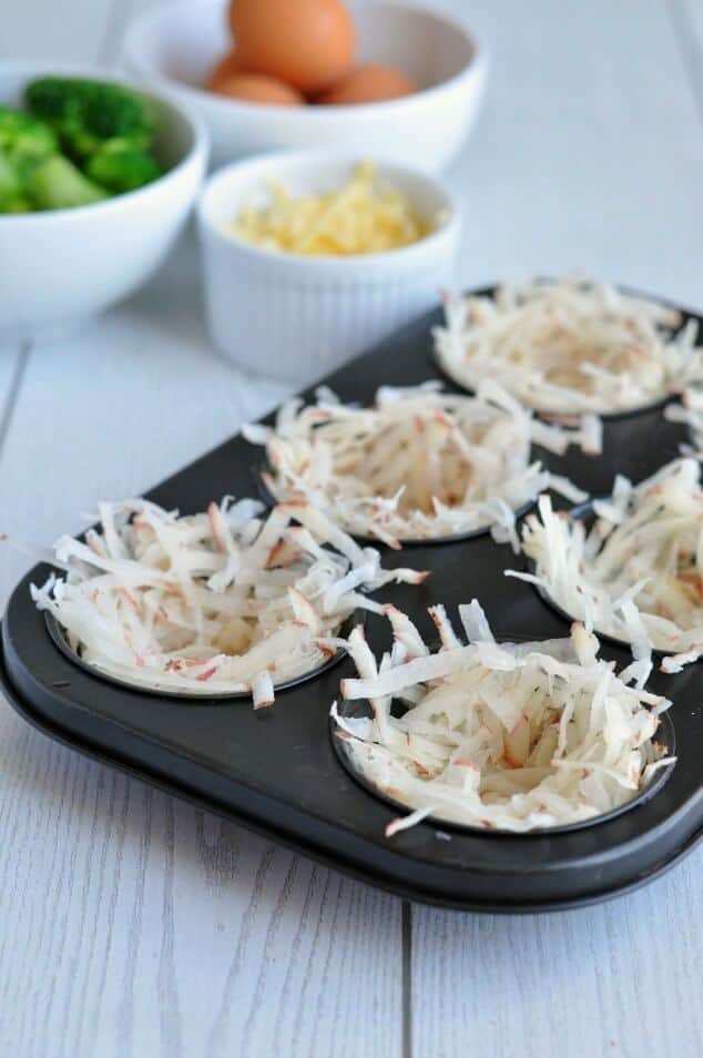 Unbaked hash browns in a black muffin tin
