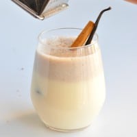 A whole nutmeg being grated into a glass of healthy eggnog
