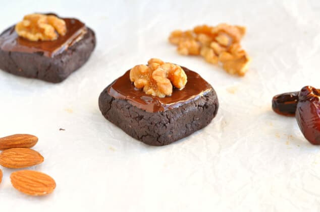 Two raw vegan brownies topped with melted chocolate and walnuts