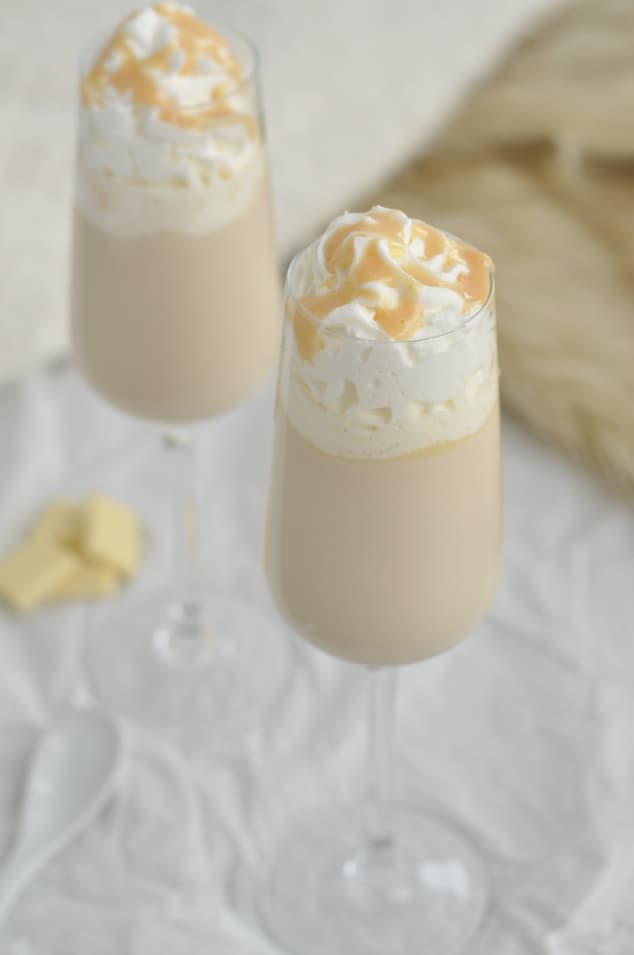 Two champagne flutes filled with Baileys cocktail and topped with cream