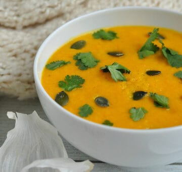 A close-up shot of a bowl of carrot and coriander soup with fresh coriander and pepitas.