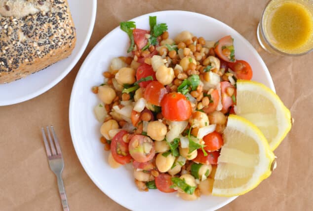 An overhead shot of lentil chickpea salad with lemon slices on a small plate.